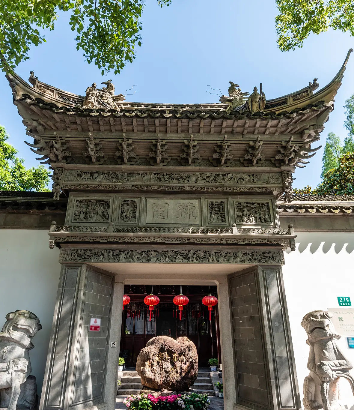 Entrance of Yuyuan Garden in Shanghai featuring traditional Chinese architecture with ornate eaves, stone lions, red lanterns, and lush greenery