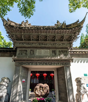 Entrance of Yuyuan Garden in Shanghai featuring traditional Chinese architecture with ornate eaves, stone lions, red lanterns, and lush greenery