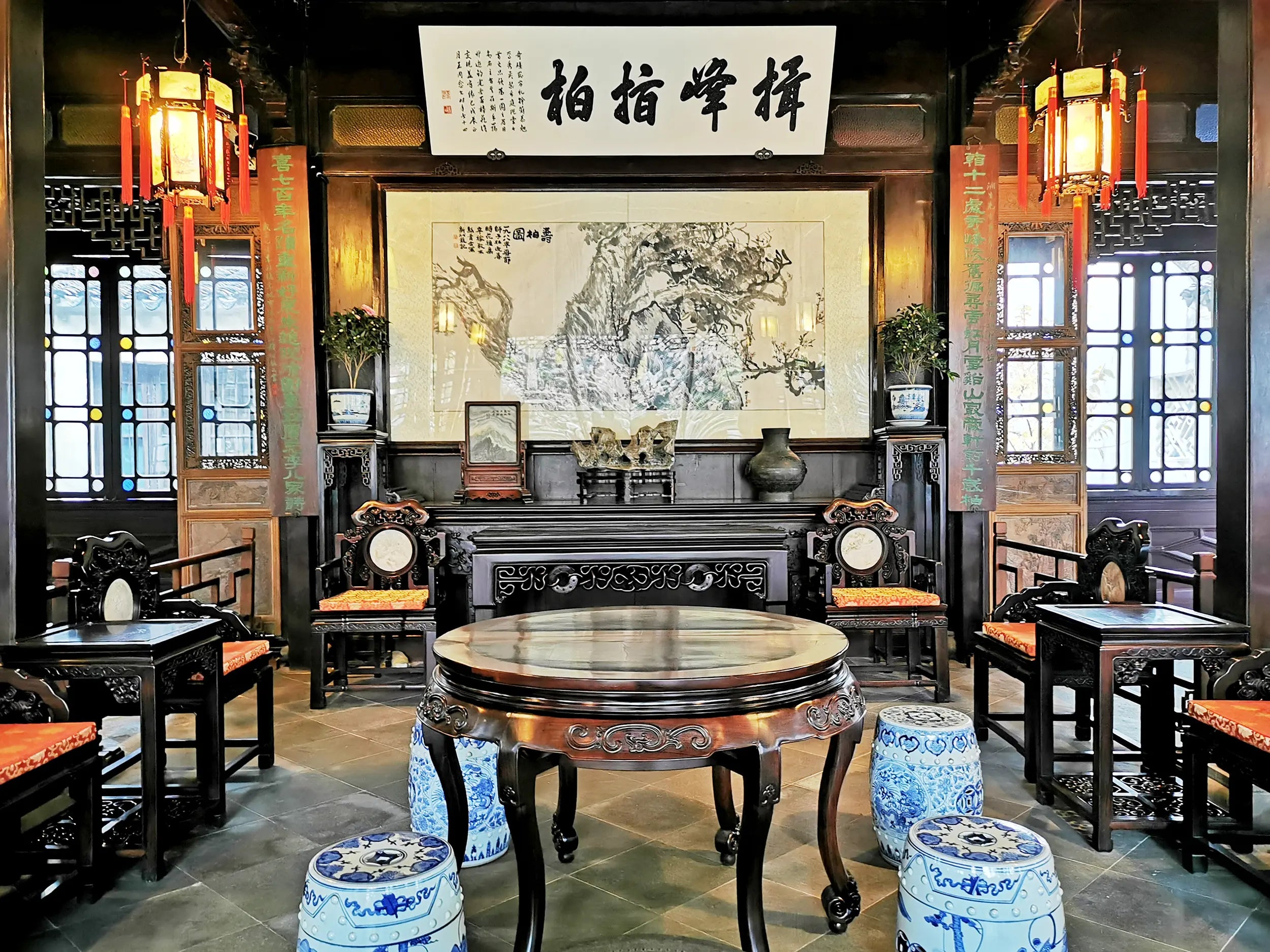 Classical Chinese courtyard interior with wooden furniture, traditional paintings, red lanterns, and natural light in Lion Grove Garden.
