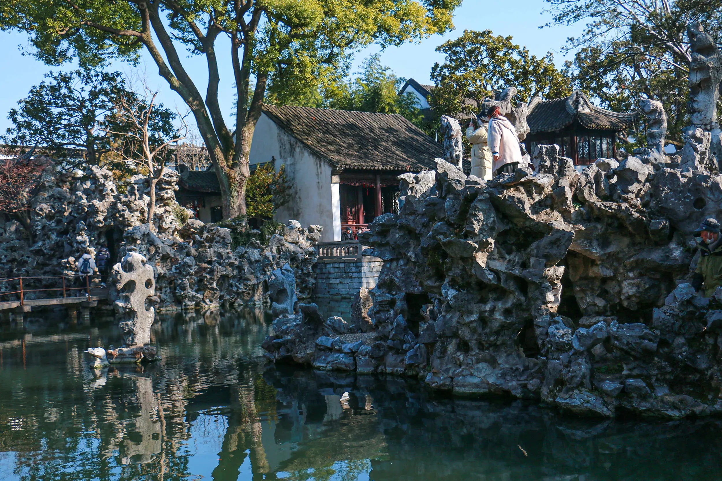 Lion Grove Garden in Suzhou with layered rockeries, a peaceful pond with ducks, and traditional Chinese architecture surrounded by lush greenery.