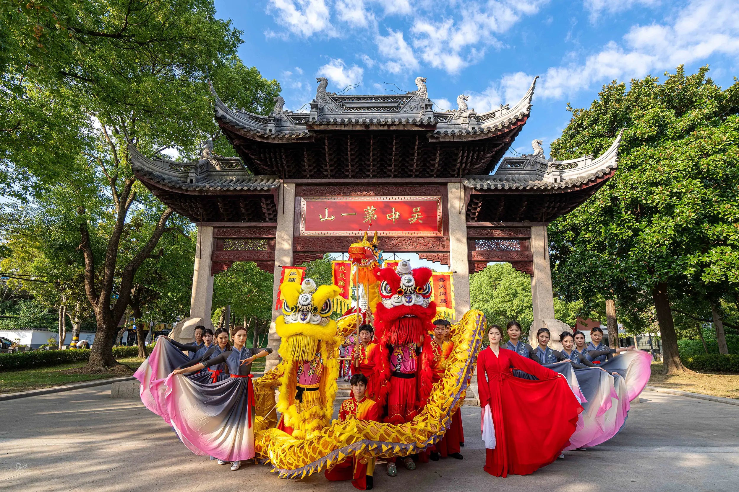 Red and yellow lion dance teams posing for a group photo at the entrance of Tiger Hill Scenic Area in Suzhou, China