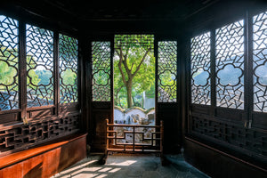 A classical Chinese room in the Humble Administrator’s Garden (Zhuozhengyuan), Suzhou. The interior features traditional wooden furniture and a stone-tiled floor in hexagonal patterns. Intricately designed lattice windows filter soft daylight while revealing glimpses of a lush green courtyard outside. The space exudes a tranquil and scholarly ambiance, evoking the refined lifestyle of ancient literati.