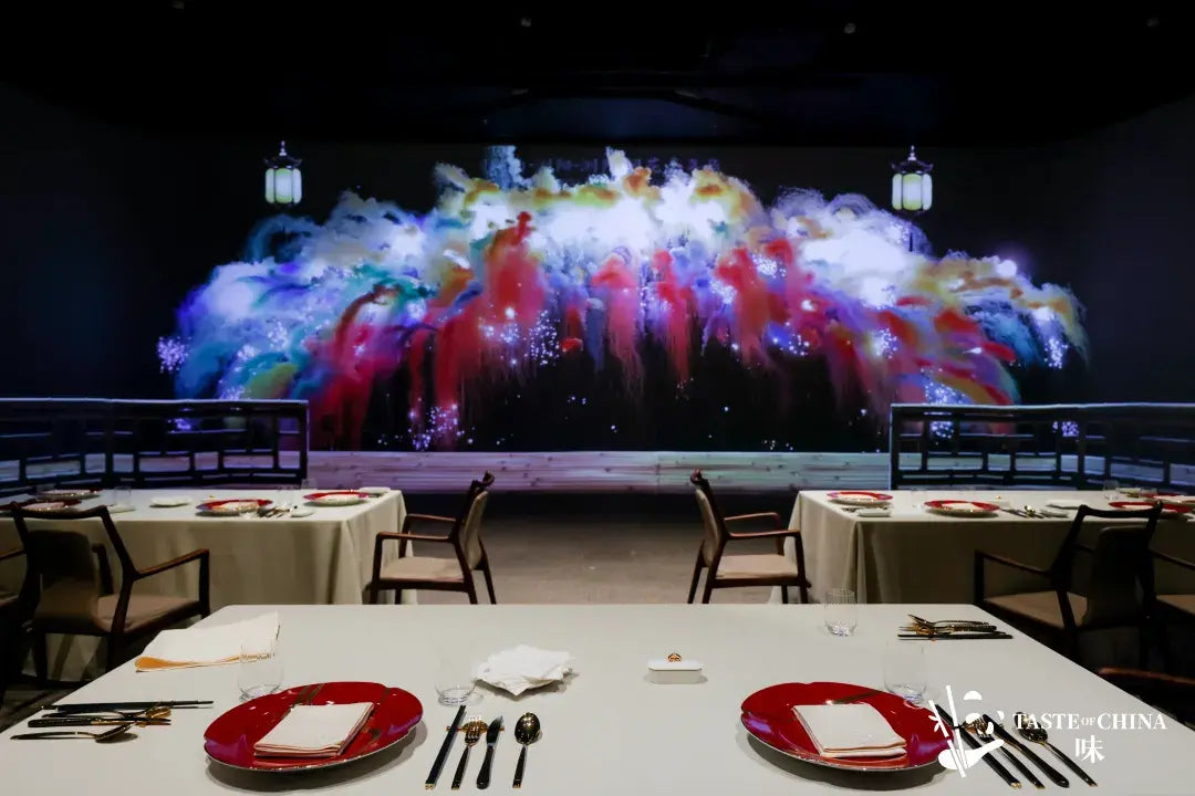 Dining table and stage with colorful smoke and light projections on the wall, creating an immersive atmosphere at The Bund, Shanghai.