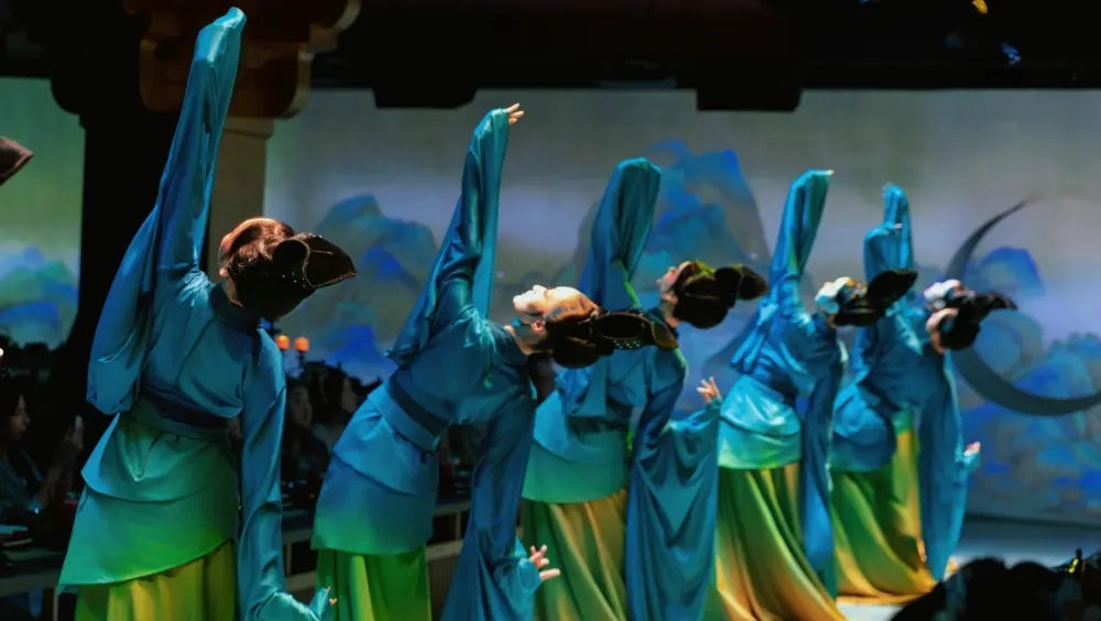 A group of women wearing blue and yellow gradient Tang-style dresses performing a traditional dance.