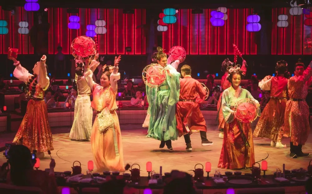 Male and female performers dressed in traditional Hanfu tossing an embroidered ball during a cultural performance.