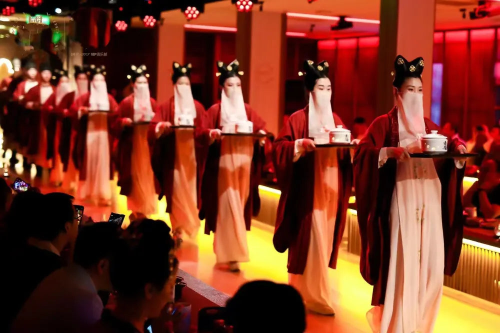 A group of women dressed in traditional Hanfu with veils, walking on stage while carrying gourmet dishes at the Shanghai immersive Han Dynasty banquet.