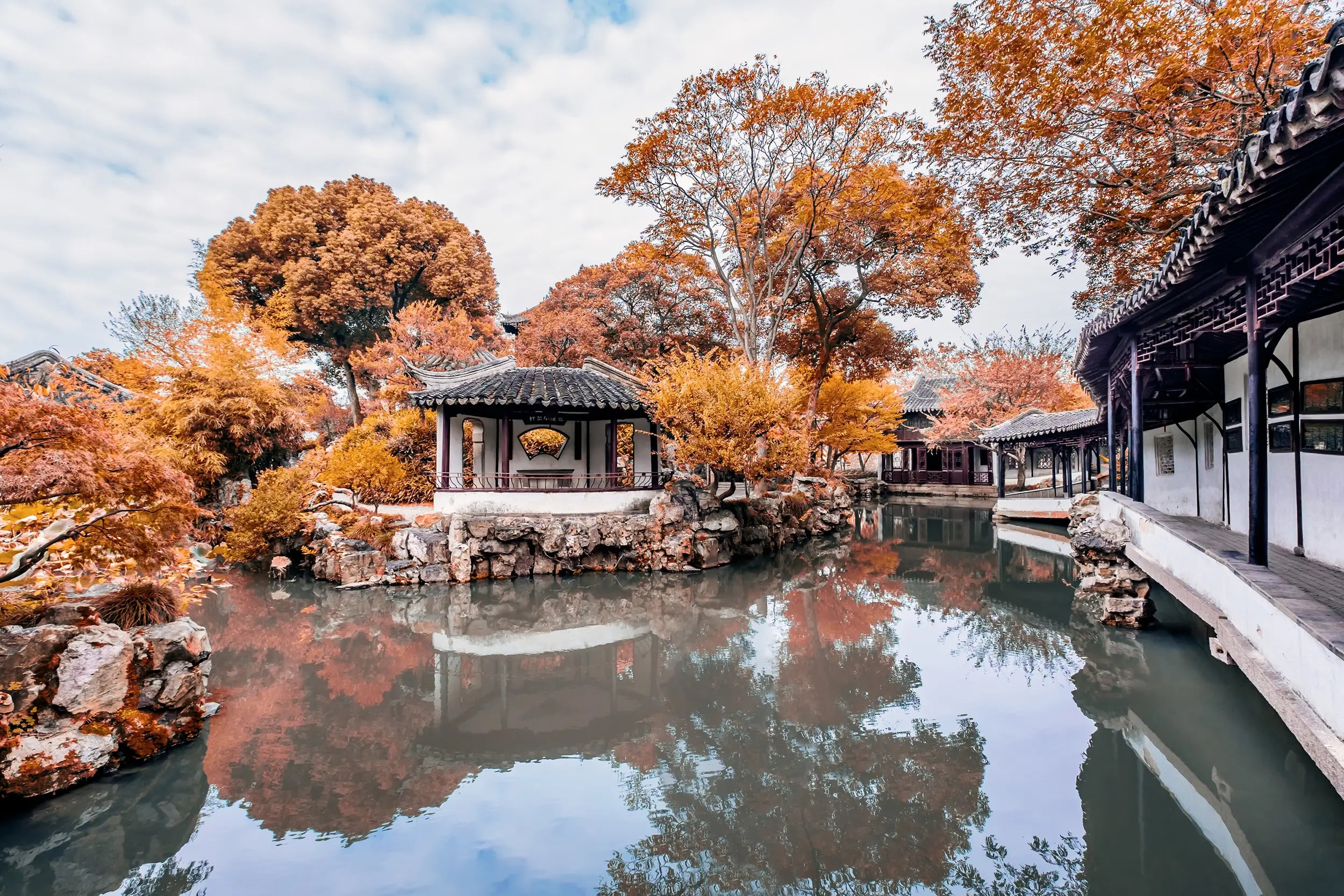 Vibrant autumn view of the Humble Administrator’s Garden, where colorful fall leaves, traditional Chinese architecture, and their reflections in the pond create a poetic, classical garden atmosphere.