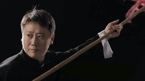 Close-up of a Kung Fu master performing with a red-tasseled spear during martial arts demonstration.