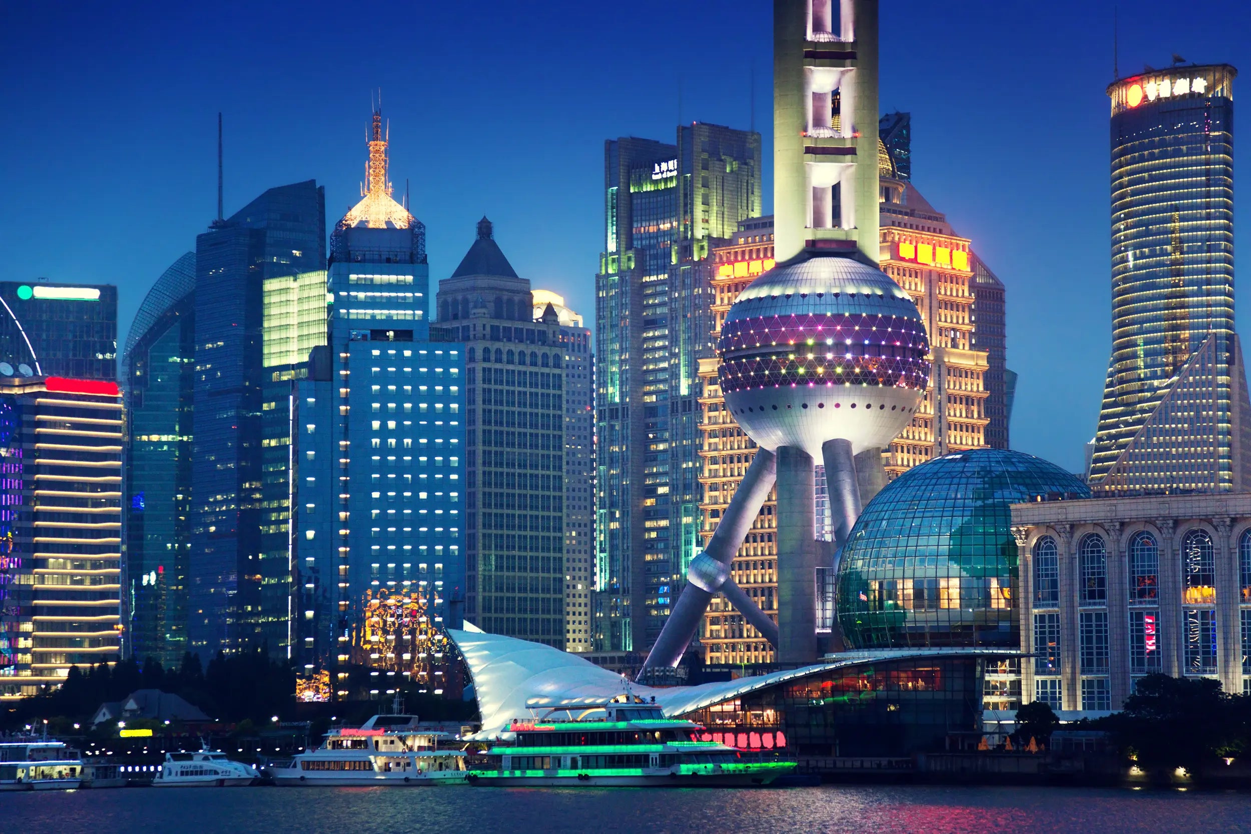 View of the Oriental Pearl Tower from a Huangpu River cruise, showing the tower's base and sightseeing boats docked along the riverside