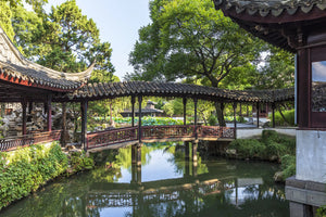 A winding zigzag corridor stretches above a clear pond, connecting pavilions and scenic spots through elegant bridges. Surrounded by lush greenery and traditional Chinese architecture, the scene embodies the tranquil charm and intricate design of Suzhou’s classical garden. Reflections on the water enhance the natural harmony and artistic depth.